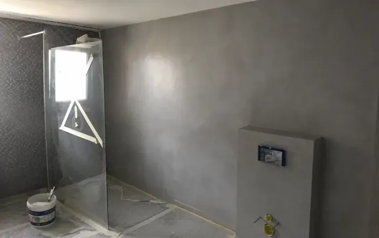 Chantier de salle de bain à Lutterbach : enduit gris en béton ciré, paroi de douche et caisson pour WC suspendus en cours d’aménagement